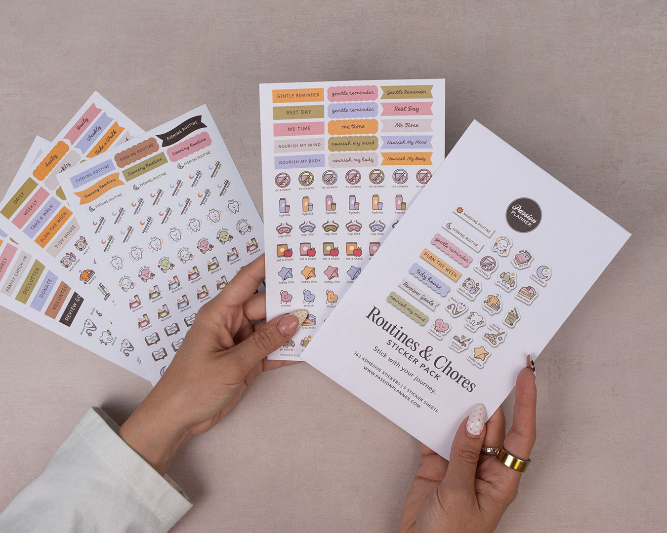 Hand holding a sheet of 'Routines & Chores' sticker pack with colorful icons on a beige background